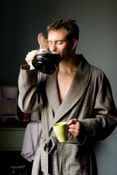 a woman drinking from a cup while wearing a robe and holding a mug in her hand