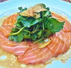 a blue plate topped with salmon and greens on top of a wooden table next to an orange slice