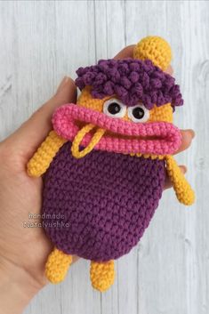 a hand holding a crocheted purple and yellow stuffed animal