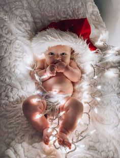 a baby wearing a santa hat laying on top of a white blanket covered in lights