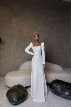 a woman in a white dress standing next to a couch and two large black rocks