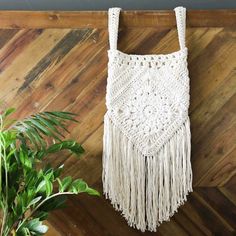 a white crocheted bag hanging on a wall next to a potted plant