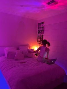 a woman is sitting on her bed with a laptop in front of her, while the lights are turned on