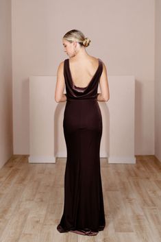 the back of a woman in a long dress standing on a wooden floor with her hands behind her back