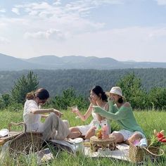 three women are sitting on the grass and having a picnic in the mountains while one woman is holding a glass of wine