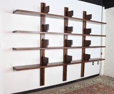 a white wall with some wooden shelves on it and a rug in front of it