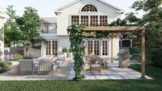 a large white house with an outdoor dining area and pergolated patio in the foreground