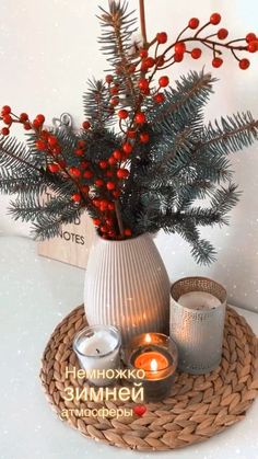 a white vase filled with red berries next to two candles on a wicker tray