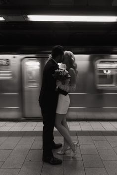 a man and woman standing next to each other in front of a subway train at night