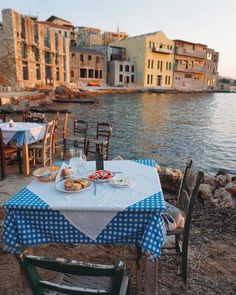 an outdoor table with blue and white checkered cloth on it next to the water