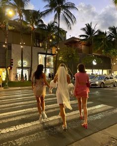 two beautiful women walking across a crosswalk in front of a building at night with palm trees