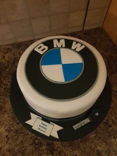 a white and black cake with blue bmw emblem on it's side, sitting on a counter top