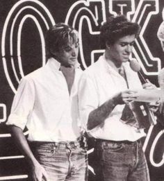 two men standing next to each other in front of a neon sign