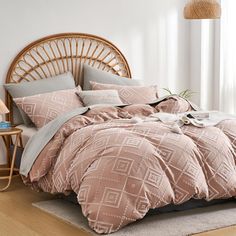 a bed with pink comforter and pillows in a room next to a wicker headboard