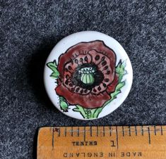 a white button with a red flower painted on it next to a ruler that is measuring