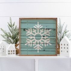 a white snowflake on a wooden sign next to small houses and pine branches