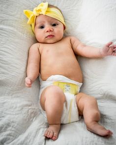 a baby wearing a yellow bow laying on top of a bed