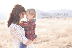 a mother holding her son in the middle of a field with mountains in the background