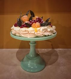 a cake with fruit on it sitting on top of a green pedestal in front of a wall