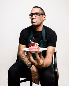 a man sitting in a chair holding a plate with a cake on top of it