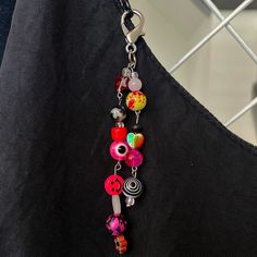 a colorful necklace hanging from a metal hook on a black piece of clothing with buttons attached to it