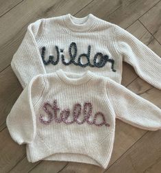 two white sweaters with the words wilder and stella written on them, sitting on a wooden floor