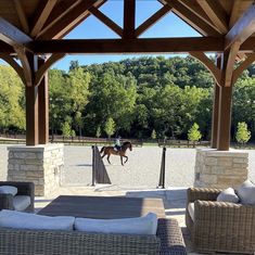 a person riding a horse in an enclosed area with wicker furniture and stone pillars