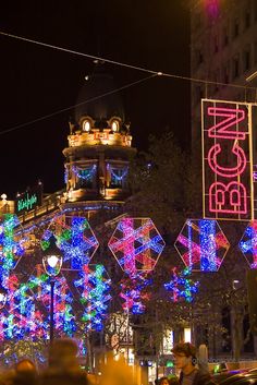 people are walking down the street in front of christmas lights and decorations on buildings at night