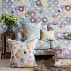 a living room filled with lots of colorful pillows and furniture next to a wall covered in patchwork