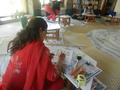 two women sitting on the floor in front of books and magazines while one woman is drawing