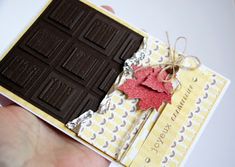 a hand holding a chocolate bar with a red leaf on it