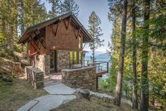 a cabin on the side of a mountain with trees around it and water in the background