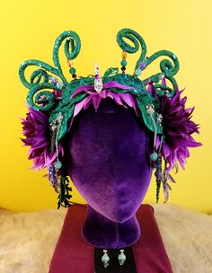 Dazzle the crowd as a magnificent fairy dragon in this purple and teal handcrafted adjustable headdress. Be the queen you were meant to be with this floral headpiece made of well crafted jewelry, glittery accents, and antennae. You are sure to turn heads at any costume party, festival, photo shoot, themed event, bachelorette party, or wedding! Let fantasy come to life with magical head-wear! D007 Mardi Gras Costume Headpiece With Adjustable Fit, Adjustable Costume Headpiece For Mardi Gras, Adjustable Headpieces For Mardi Gras Costume, Fantasy Headpieces For Mardi Gras Costume, Whimsical Headpieces With Matching Headband For Costume Party, Whimsical Crown Costume Hats And Headpieces For Parties, Whimsical Headband For Costume Party, Fantasy Style Headband For Masquerade, Whimsical Headpieces For Festivals And Parties