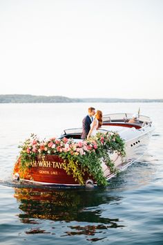 a bride and groom kissing on the back of a boat with flowers growing out of it