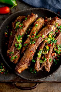 some meat is sitting in a pan with vegetables on the side and peppers around it