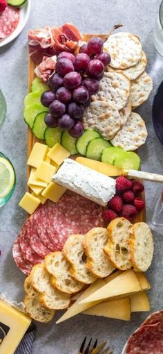 an assortment of cheeses, meats and fruit on a platter with crackers