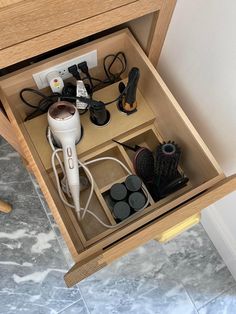 an open drawer with hairdryers and other items in it on the floor next to a wall