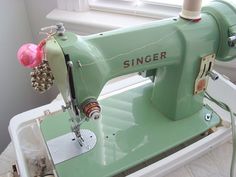 an old green sewing machine sitting on top of a table next to a white window