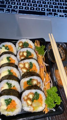 sushi and chopsticks on a tray with a laptop in the background