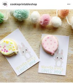 two decorated cookies sitting on top of a table next to pom poms and paper