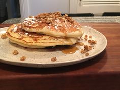 a stack of pancakes sitting on top of a white plate covered in syrup and nuts