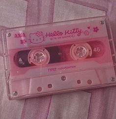 an old hello kitty tape recorder is laying on a pink bed sheet with the words hello kitty printed on it