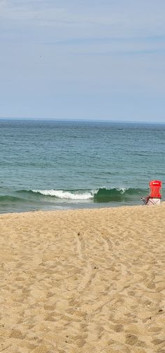 a red chair sitting on top of a sandy beach next to the ocean with waves coming in