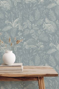 a white vase sitting on top of a wooden table next to a blue wallpaper