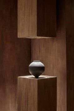 a black vase sitting on top of a wooden block in the middle of a room