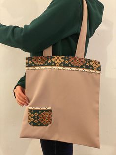 a woman holding a beige and brown bag with an embroidered pocket on the side,