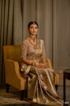 a woman sitting in a chair wearing a gold and silver sari with pearls on her head