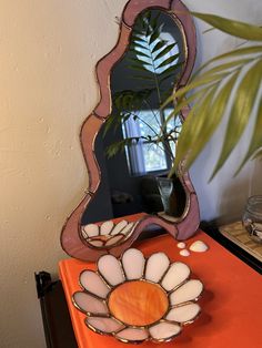 a mirror sitting on top of an orange table next to a potted palm tree