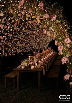 a long table with candles and flowers on it is lit up in the night sky