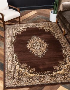 a brown area rug with an ornate design on the center and sides, in front of a white chair